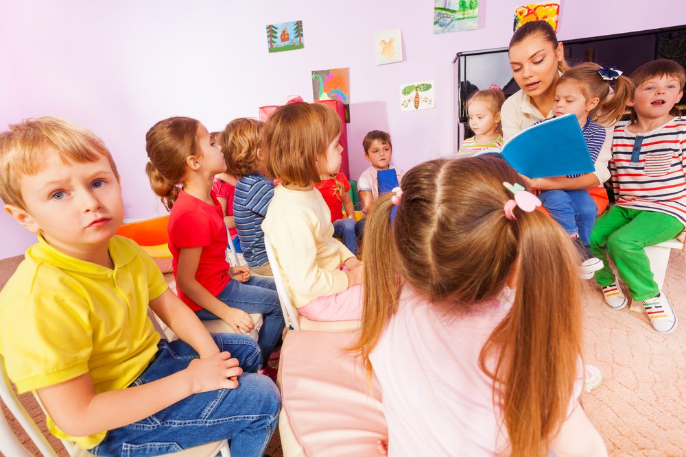 A diverse group of children sitting attentively in a classroom, listening to their teacher during a lesson.